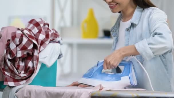 Веселая домохозяйка в хорошем настроении гладит футболку, наслаждается домашней работой, крупным планом — стоковое видео