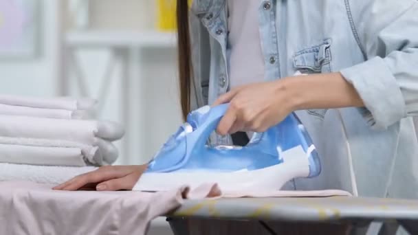 Недовольная домохозяйка делает дырку в футболке во время глажки, недостаток опыта — стоковое видео