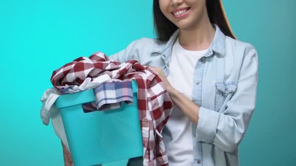 Щаслива домогосподарка тримає кошик з одягом і посміхається на камеру, пральня — стокове відео