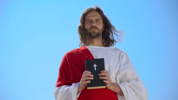 Суворий Бог тримає Біблію проти синього неба, нагадуючи про віру і покаяння — стокове відео