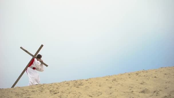 Иисус с тяжелым деревянным крестом, едва ходящим, библейская история распятия — стоковое видео