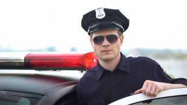 Güvenli polis memuru üniformalı ve güneş gözlüğü devriye arabası yakınında ayakta