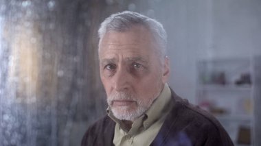 Yalnız üzgün Büyükbaba yağmurlu pencere, hemşirelik ev aracılığıyla kamera bakıyor