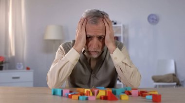 Masa üzerinde renk yapı taşları bakarak Pensive yaşlı adam, yaşlı demans