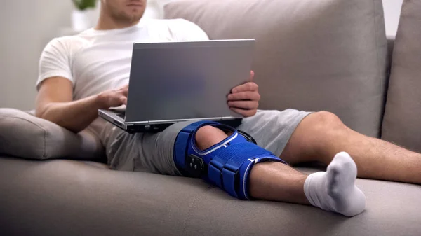 男子在关节炎膝部支架工作在笔记本电脑在家里康复期间和自由职业 — 图库照片