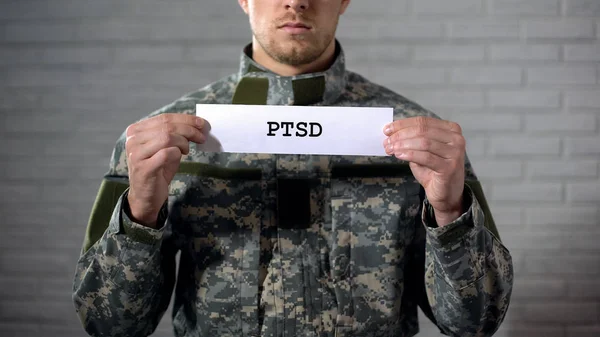 PTSD written on sign in hands of male soldier, posttraumatic disorder, health