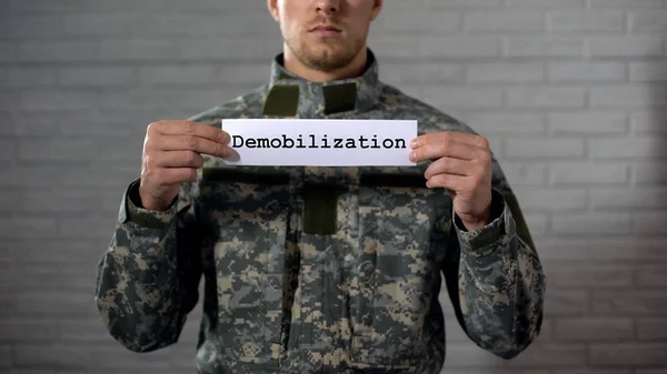 Demobilization word written on sign in hands of male soldier, end of term