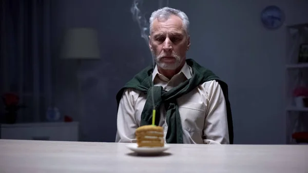 不开心的老人看着蛋糕和吹蜡烛 悲伤的生日 — 图库照片
