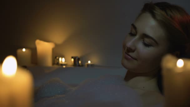 Jeune femme appréciant le bain avec des bulles de mousse et des bougies, soirée détente, gros plan — Video
