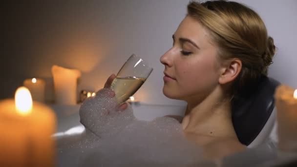 Ονειρεμένη γυναίκα που βρίσκεται στο μπάνιο με φυσαλίδες αφρού και κεριά, πίνοντας σαμπάνια — Αρχείο Βίντεο
