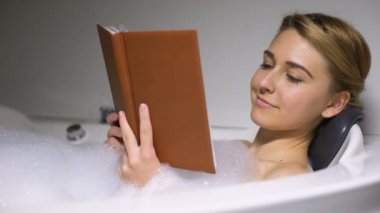 Köpük kabarcıkları ile banyoda kitap okuyan rahat kadın, evde akşam, yakın çekim