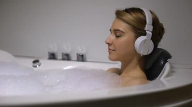 Kulaklıklı kadın köpük kabarcıkları ile banyoda ürpertici, yavaş müzik dinlerken