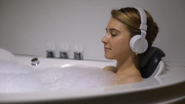 Donna in cuffia agghiacciante in bagno con bolle di schiuma, ascoltando musica lenta — Video Stock