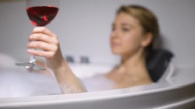 Köpük kabarcıkları ile banyoda şarap içen sevimli kadın, zor bir günün ardından rahatlatıcı