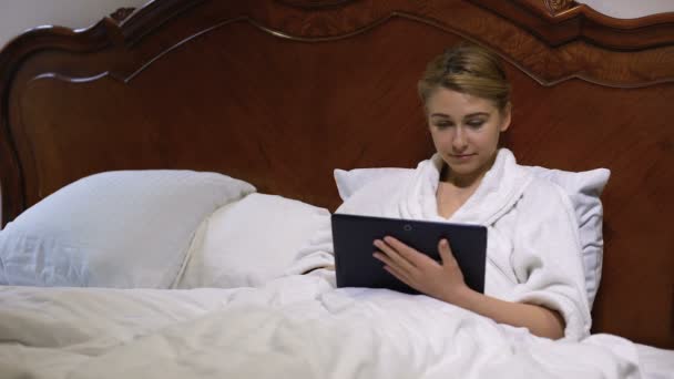 Mujer sonriente acostada en la cama desplazándose en la tableta PC, charlando en la red social — Vídeos de Stock