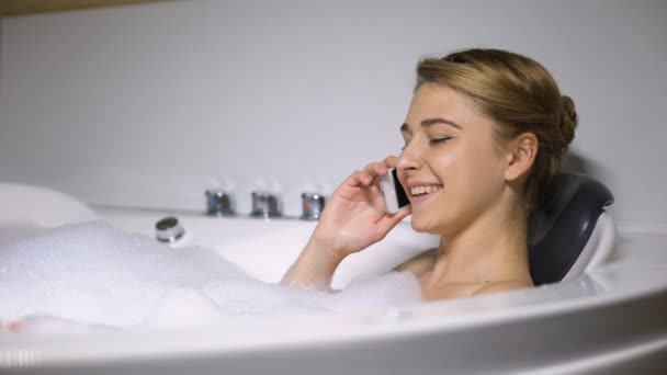 Флиртующая женщина разговаривает по телефону, наслаждается ванной с пеной пузырьков, разговор — стоковое видео