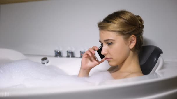 Upset woman talking phone in bath with foam bubbles, negative news, close-up — Stock Video