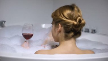Köpük kabarcıklar, sağlıklı yaşam ve spa ile banyoda şarap içme sevimli kadın, rahatlayın