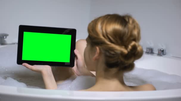 Женщина в ванной держит планшетный компьютер, смотрит онлайн видео канал, вид сзади — стоковое видео