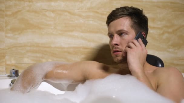 Anger man quarrelling with girlfriend on mobilephone, taking relaxing foambath — Stock Video