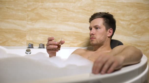 Нервный бизнесмен пытается расслабиться, принимая ванну с ароматом и выпивая ром — стоковое видео