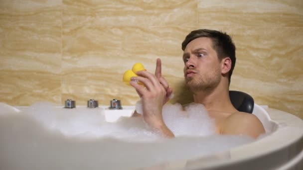 Lustiger Typ, der in der Badewanne mit Gummienten spielt und sich an die Kindheit erinnert — Stockvideo