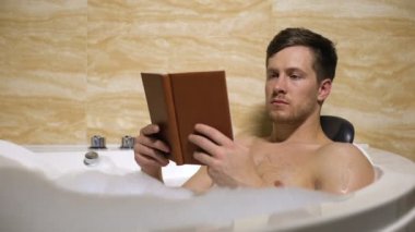 Adam köpük ile rahat banyoda rahatlatıcı ve ilginç kitap okuma zaman harcama