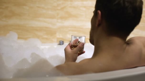 L'uomo riposa e si rilassa nella comoda vasca da bagno bevendo whisky con ghiaccio, spa — Video Stock