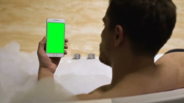 Мужчина смотрит сериал на смартфоне принимая ванну с пеной, досуг, 4g интернет — стоковое видео
