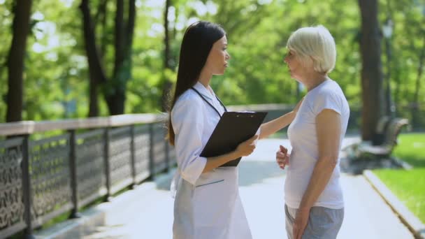 Vecchia donna che si lamenta di mal di cuore alla giovane infermiera nel parco ospedaliero, assistenza sanitaria — Video Stock