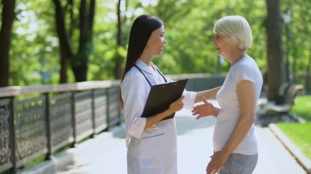 Enfermera joven hablando con anciana en el parque del centro de rehabilitación, atención médica — Vídeo de stock