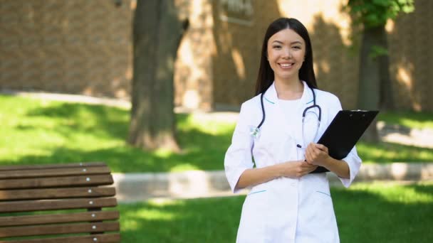 Verpleegster in uniform staande in Hospital Park, glimlachend op camera, medische zorg — Stockvideo