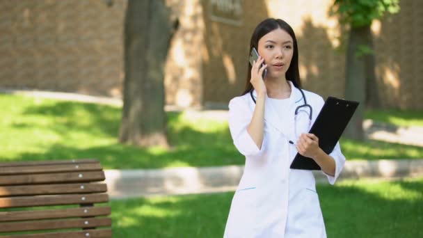 Lachende verpleegster praten telefoon met patiënt in ziekenhuis Park, medische zorg, gezondheid — Stockvideo