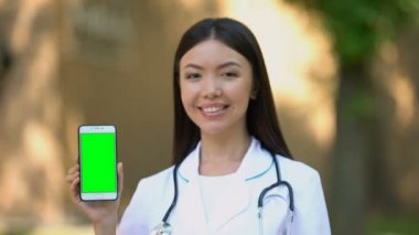 Gülümseyen kadın doktor kamera, sağlık yeşil ekran ile akıllı telefon gösteren