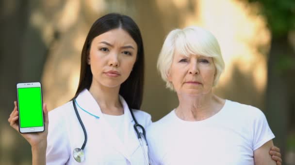 Krankenschwester mit altem Patienten zeigt Smartphone mit grünem Bildschirm vor Kamera — Stockvideo