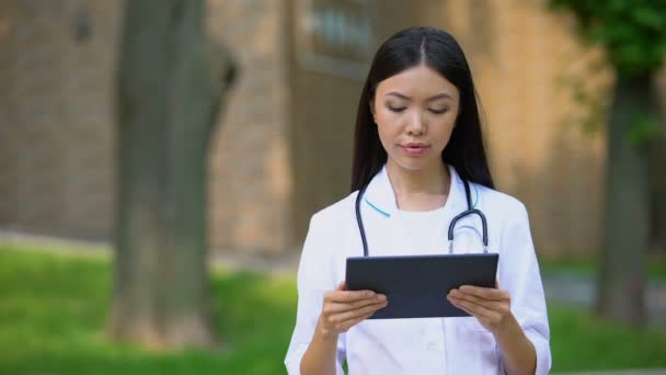 Kvinnlig sjuksköterska kontrollundersökning resultat på Tablet PC, Hospital Park, hälsa — Stockvideo