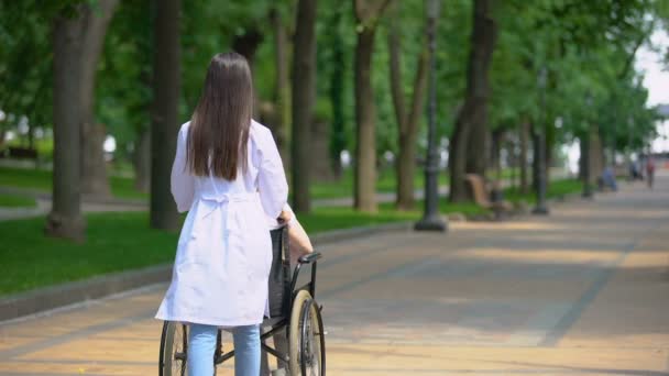 Enfermera caminando en parque con paciente discapacitada, centro de rehabilitación — Vídeos de Stock