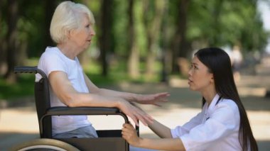 Hastane parkında tekerlekli sandalyede üzgün yaşlı kadın destekleyen kadın gönüllü
