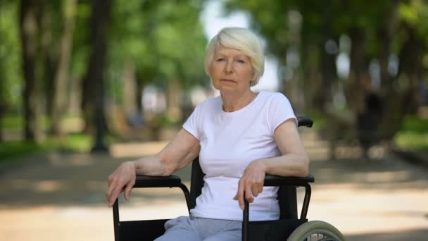 Femme âgée frustrée en fauteuil roulant regardant à la caméra dans le parc de l'hôpital — Video