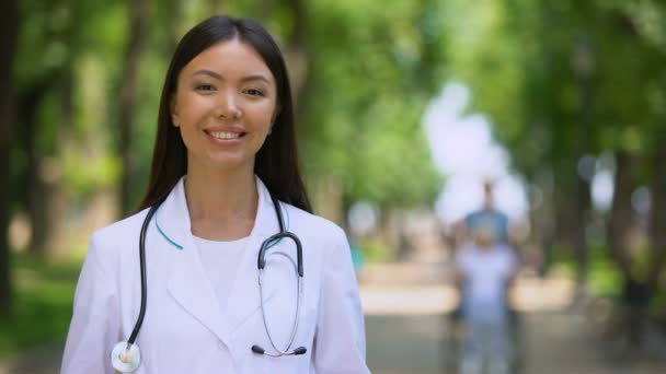 Alegre terapeuta femenina sonriendo en la cámara en el parque del hospital, al aire libre — Vídeo de stock