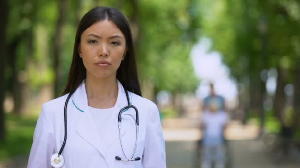 Médico femenino serio mirando en cámara en el parque del centro de rehabilitación, salud — Vídeo de stock