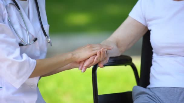 Terapeuta mujer de la mano de una anciana discapacitada en silla de ruedas, al aire libre — Vídeos de Stock