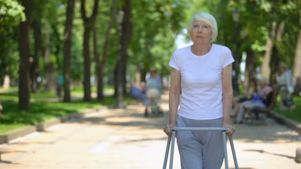 Mujer vieja trastornada que se mueve al aire libre con el marco que camina, rehabilitación después del trauma — Vídeo de stock