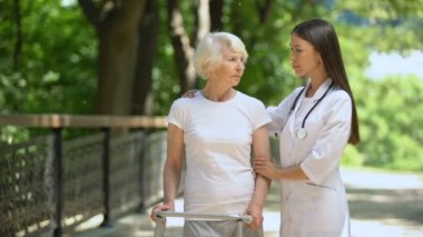 Yürüyüş çerçevesi ve kadın terapist kameraya bakarak üzgün yaşlı kadın