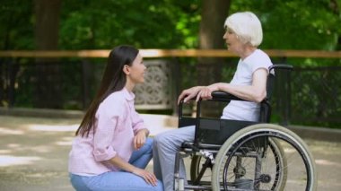 Tekerlekli sandalyede yaşlı kadınla konuşan gülen gönüllü, engellilere destek