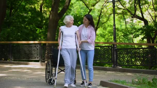 Koltuk değnekleriyle yürüyen yaşlı kadına yardım genç kadın, kalça kırığı rehabilitasyonu — Stok video