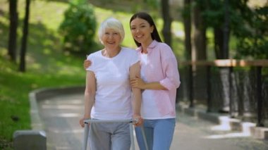 Genç kadın yürüyüş çerçevesi açık havada yaşlı kadın sarılma, rehabilitasyon