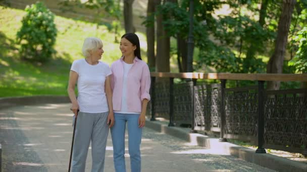 Внучка разговаривает с пожилой женщиной ходить с палкой в парке, здоровье старости — стоковое видео