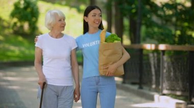 Sosyal gönüllü baston ile yaşlı kadın destekleyen bakkal çantası tutarak