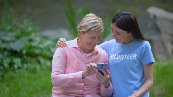 Mogen kvinna och ung volontär söker smartphone foton tillsammans, hjälp — Stockvideo